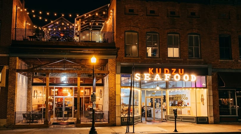 Kudzu Seafood restaurant exterior at night, with string lights illuminating the patio and balcony.