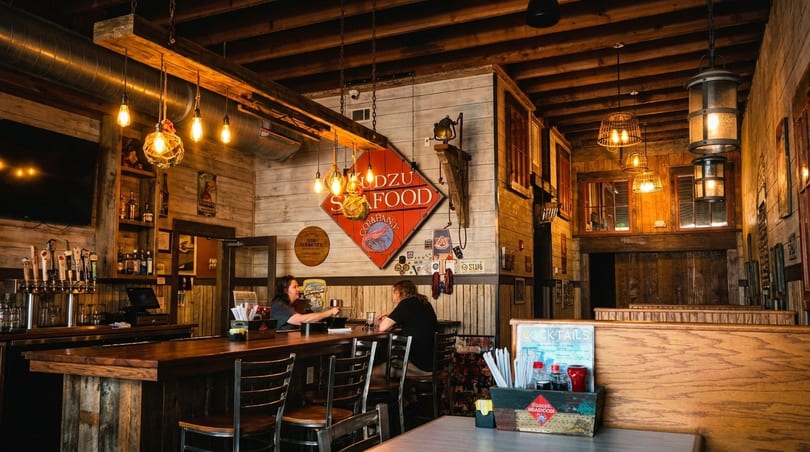 Two women seated at a rustic wooden bar in a restaurant with warm lighting and wood paneling.