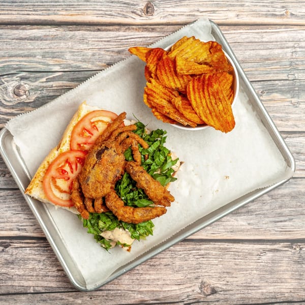 Fried soft-shell crab po'boy with lettuce, tomato, and a side of seasoned potato chips.