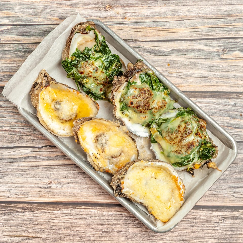 Baked oysters on a metal tray, some with cheese and some with spinach and cheese.