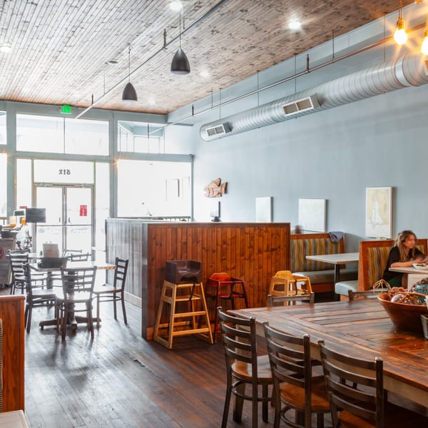 Spacious restaurant interior with wooden tables, booths, and a couple dining, featuring exposed ductwork and ceiling.