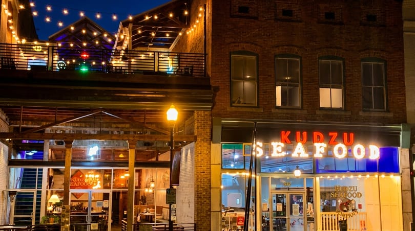 Exterior of Kudzu Seafood restaurant at night, with illuminated signs and string lights on a patio.