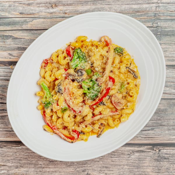 Creamy macaroni and cheese with broccoli, red bell peppers, and mushrooms on a white plate.