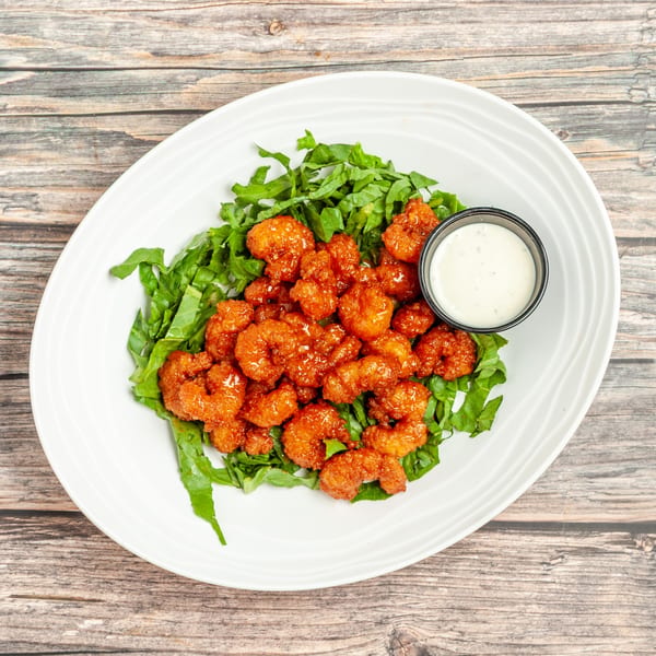Crispy orange shrimp on a bed of green lettuce with a side of white dipping sauce.