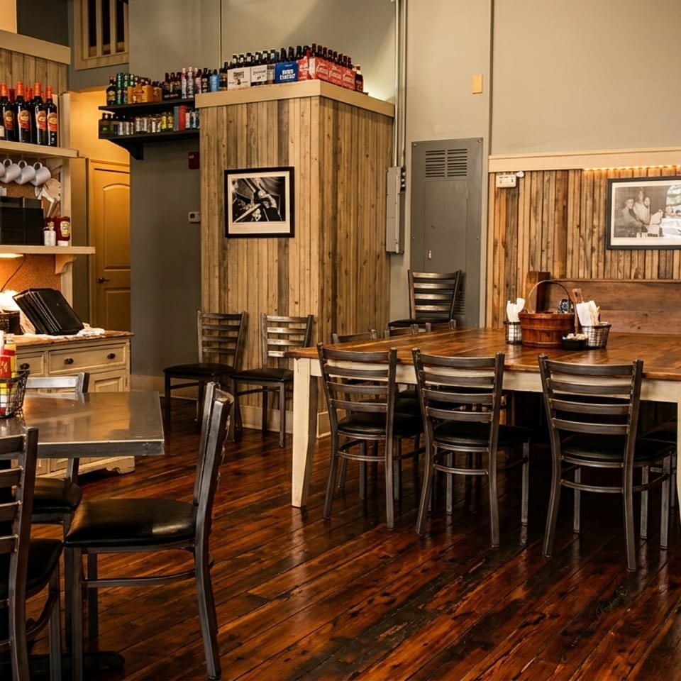 Rustic restaurant interior with wooden tables, chairs, and wall paneling, featuring framed pictures and bottles.