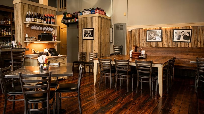 Rustic restaurant interior with wooden walls, dark wood floors, and tables set for dining.