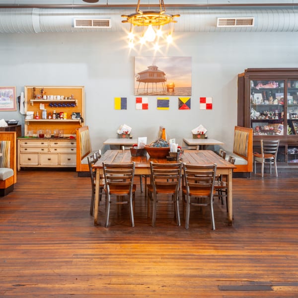 Restaurant interior with wooden floors, nautical decor, booths, and a large communal table.