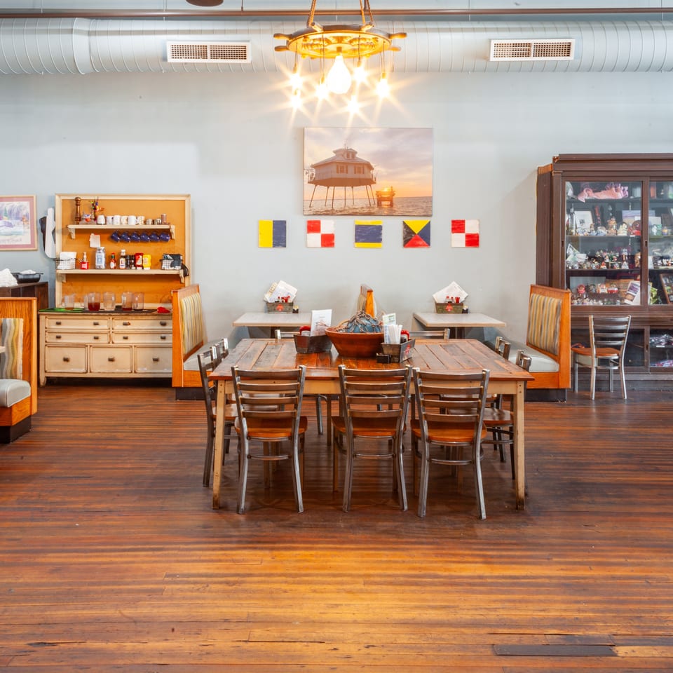 Restaurant interior with wooden floors, nautical decor, booths, and a large communal table.