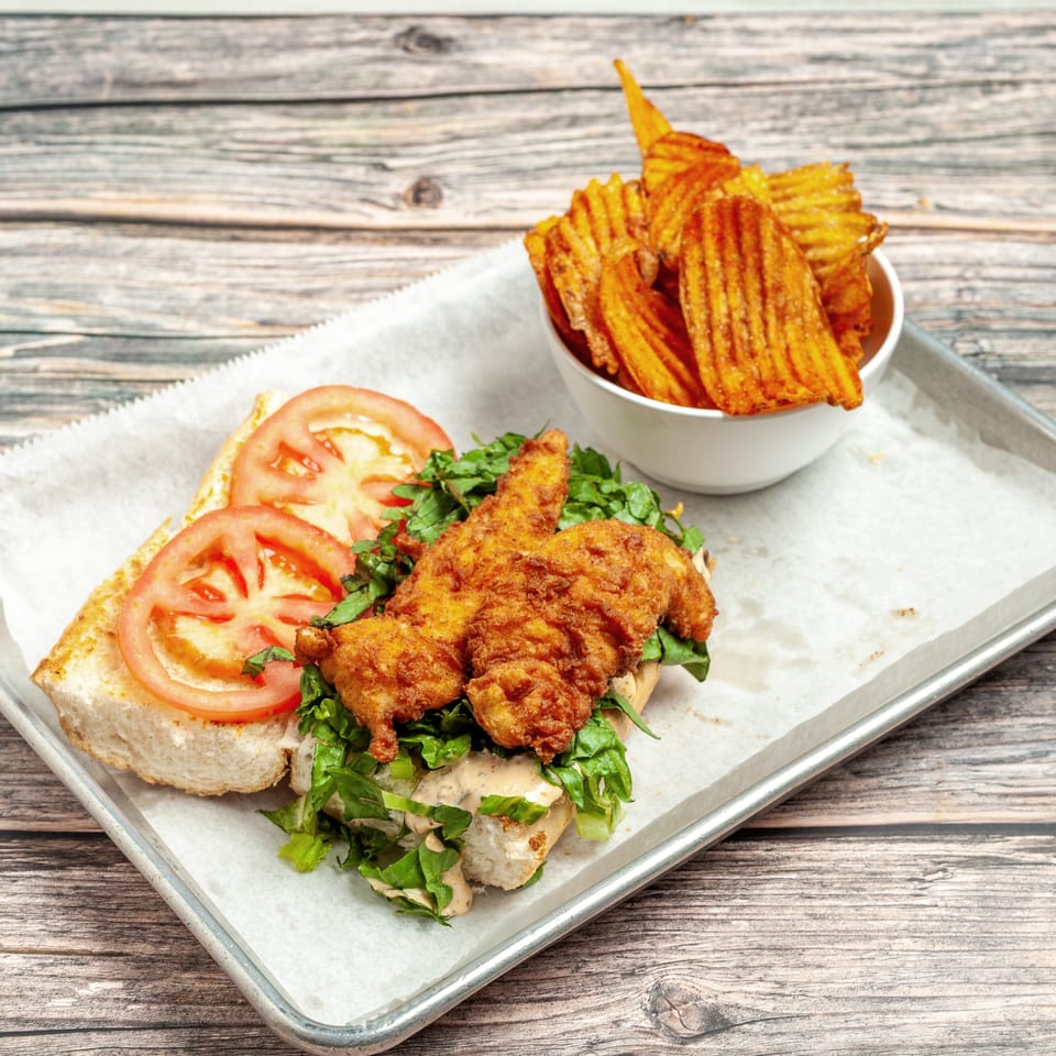 Crispy fried chicken sandwich with lettuce, tomato, and sauce, served with waffle fries on a tray.