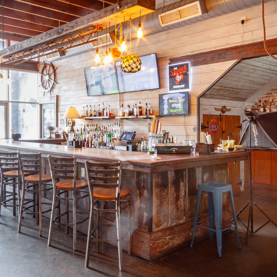Rustic bar with stools, liquor bottles, TVs, and nautical decor in a restaurant.