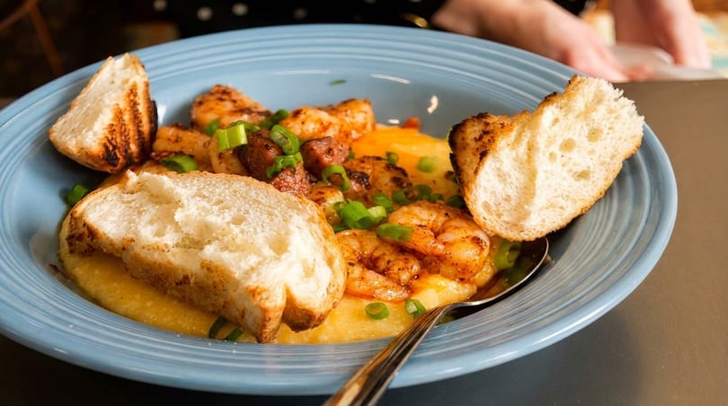 Shrimp and grits with sausage, green onions, and toasted bread in a blue bowl.