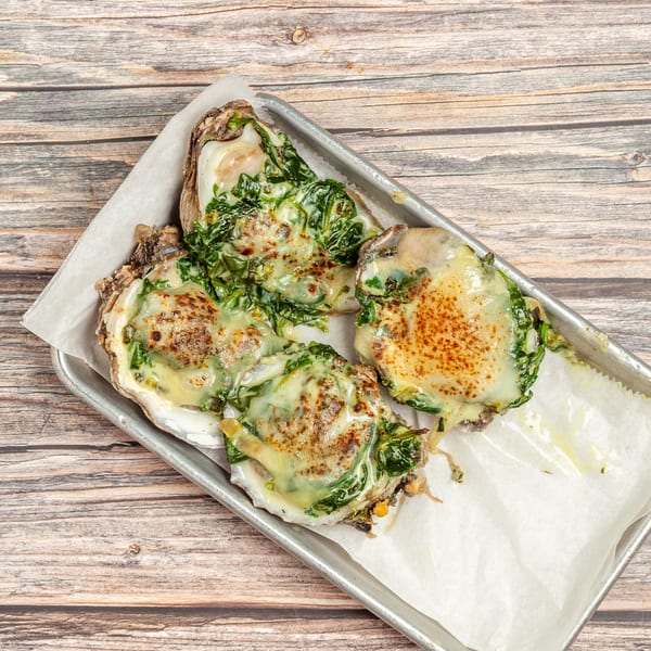Four baked oysters topped with melted cheese and spinach, served on a metal tray.