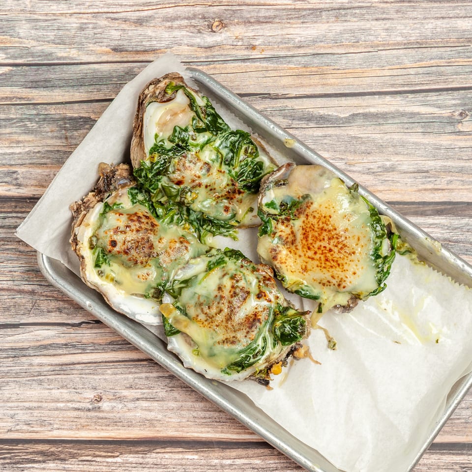 Four baked oysters topped with melted cheese and spinach, served on a metal tray.