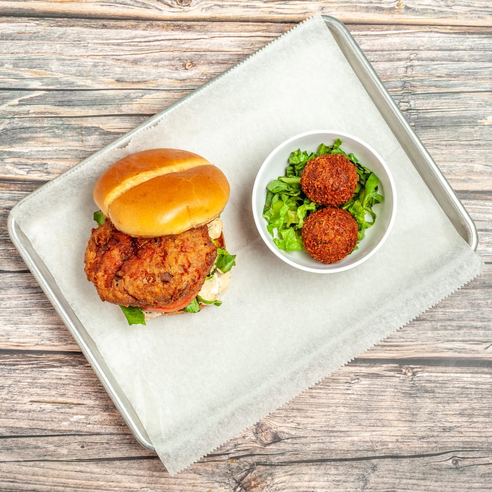 Crispy fried chicken sandwich with lettuce, tomato, and sauce, served with two falafel balls on lettuce.